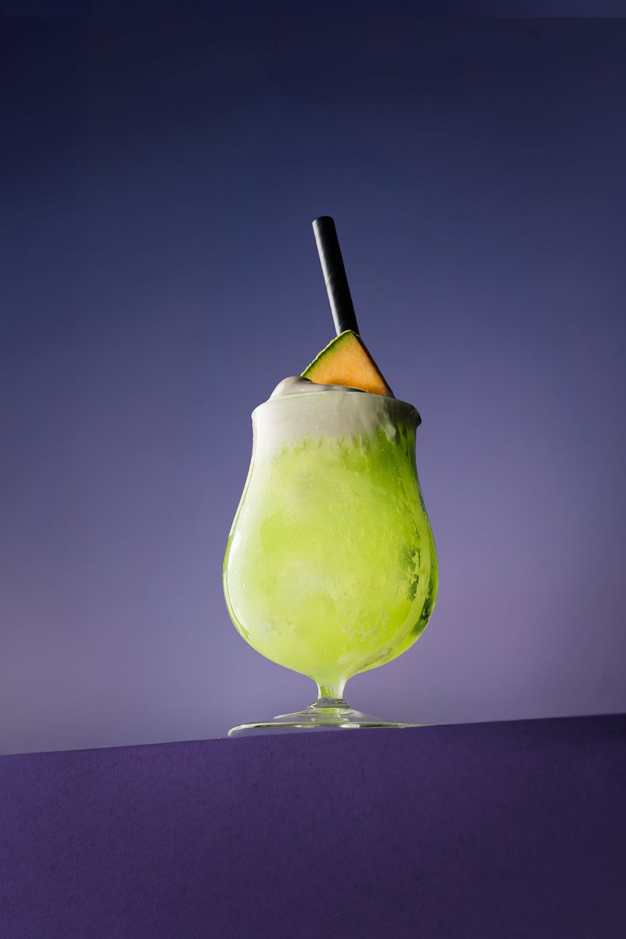 Melon Spider in a hurricane glass with a melon wedge, on purple