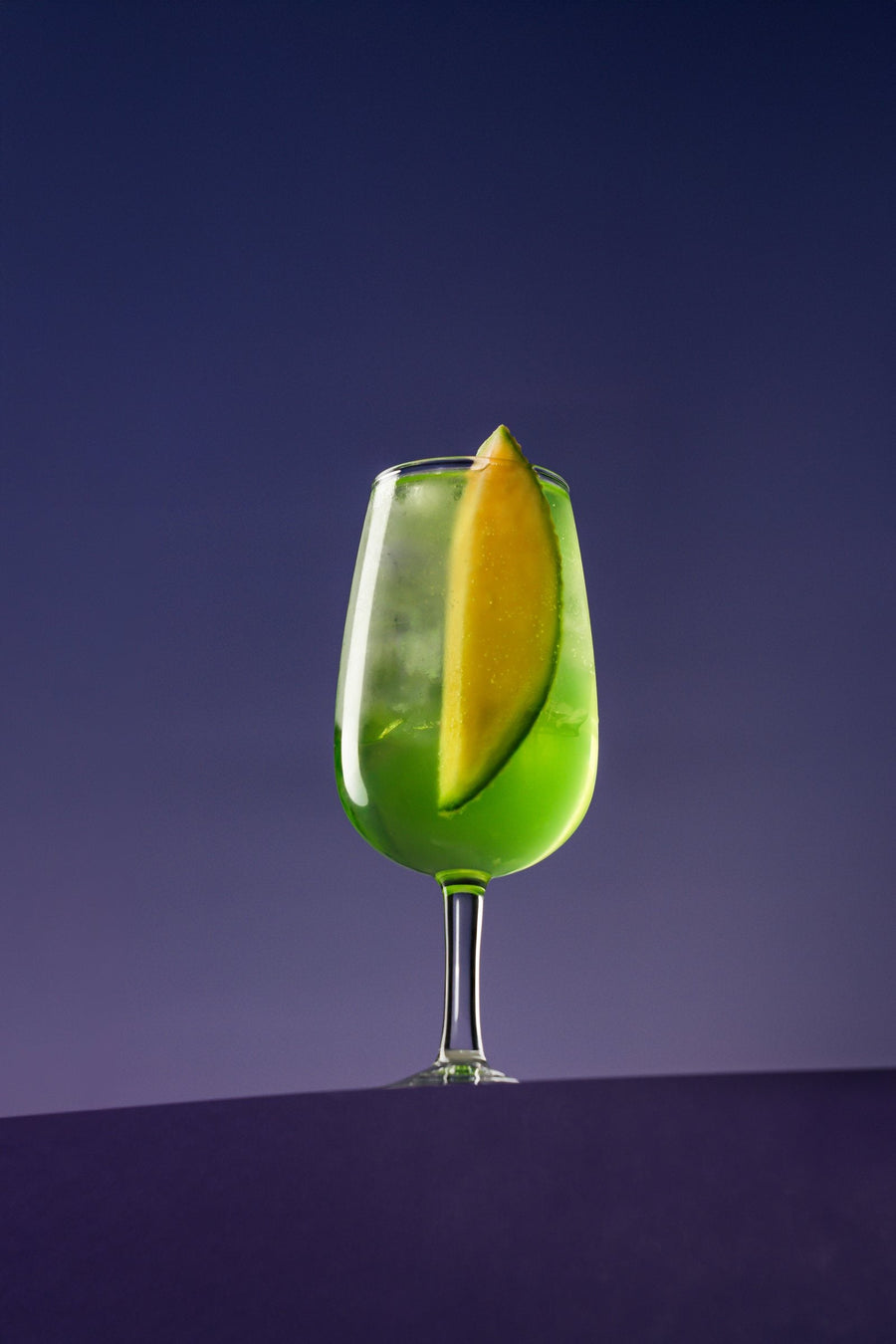 Melon Spritz in a wine glass with a melon wedge, on purple