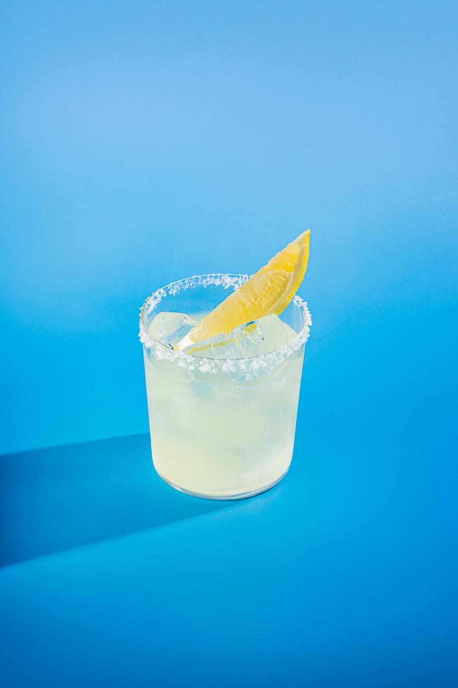 Lemon Marg in a salt-rimmed rocks glass with a lemon wedge, on blue