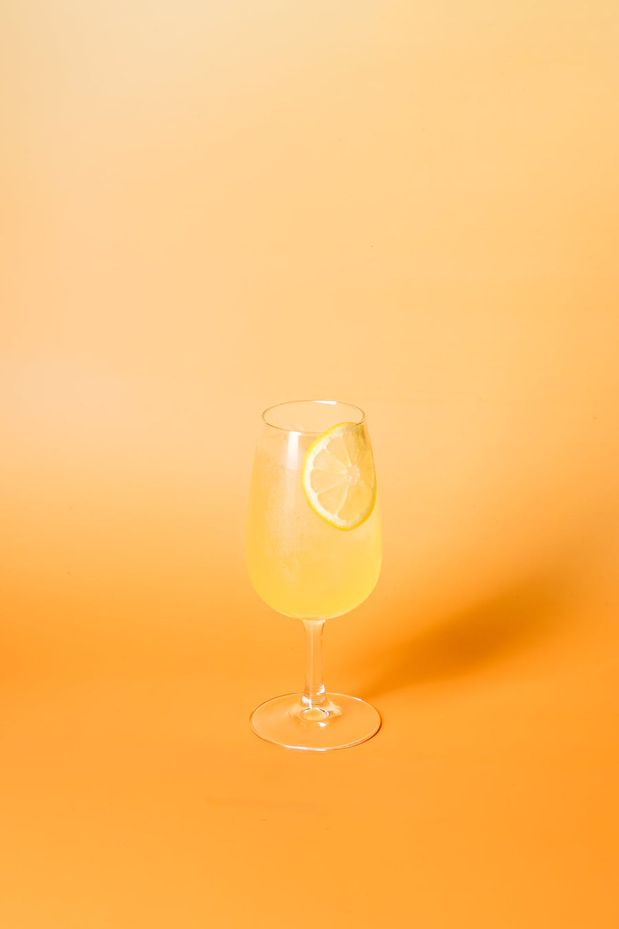 Lemon Spritz in a wine glass with a lemon wheel, on orange